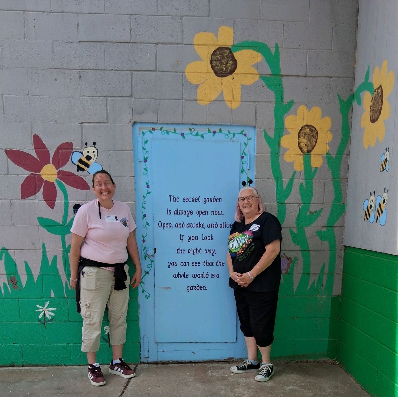 Two volunteers in front of a painted garden door