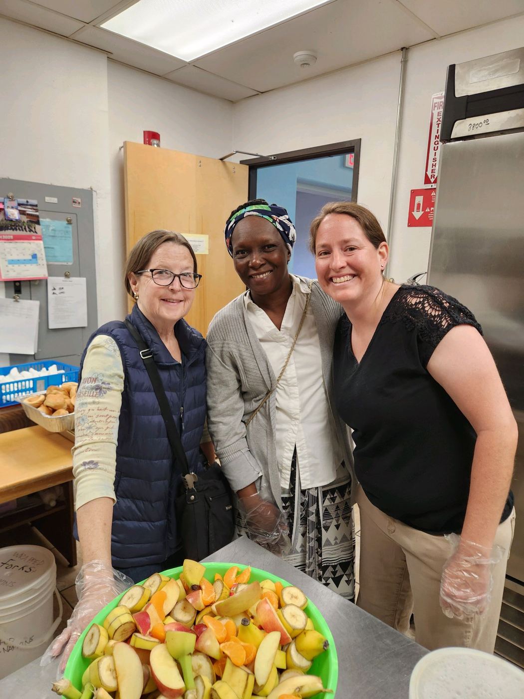 Three kitchen volunteers with a bowl of fresh fruit